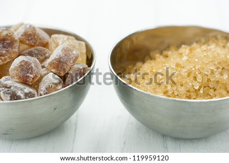 rock candy and brown sugar piles in steel bowls, white wood table background