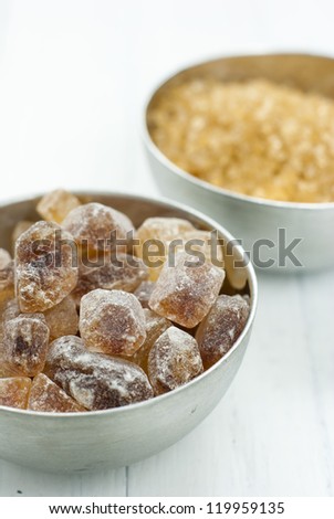 rock candy and brown sugar piles in steel bowls, white wood table background