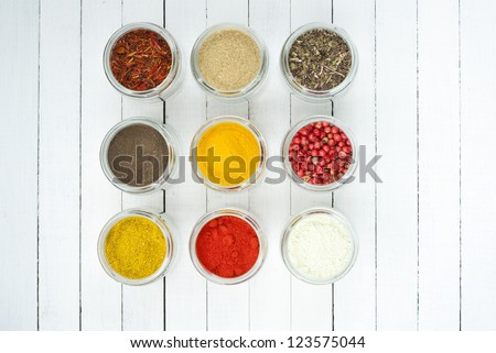 spices in glass jars on white wooden table, top view