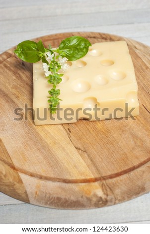 cheese on wooden board with blossoming basil and garlic cloves, bright wooden table