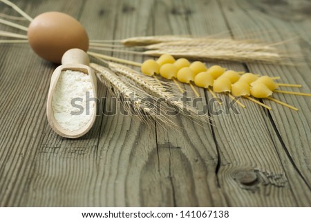 wheat ears, egg and flour on wooden spoon, wood table