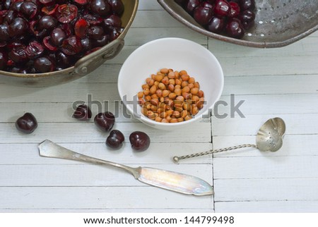 cherry fruits in a metal bowl and seeds on white wood table