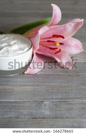 cosmetic cream and pink lily flower on weathered wooden table background