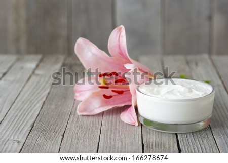 cosmetic cream and pink lily flower on weathered wooden table background