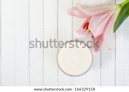 cosmetic cream and pink lily flower on white wooden