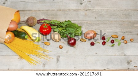 raw fruits and vegetables, pasta and eggs rolling from paper bag on weathered wooden table