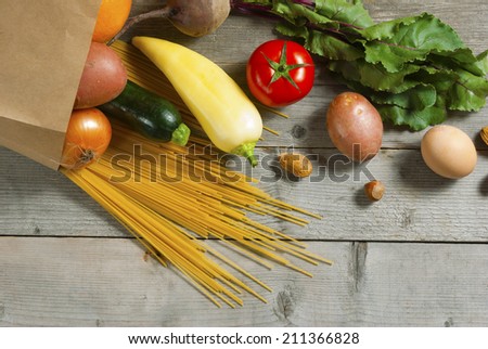 raw fruits and vegetables, pasta and eggs rolling from paper bag on weathered wooden table