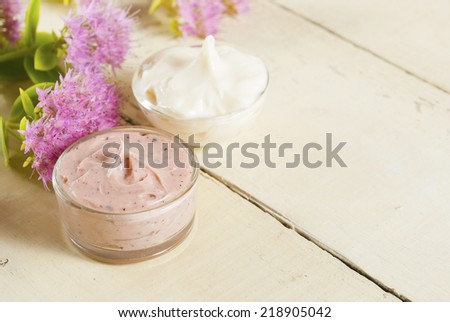 hand and face cream with pink flowers on bright, rusty wooden