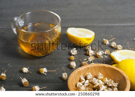 cup of chamomile tea with dried flowers and lemons on black wood table
