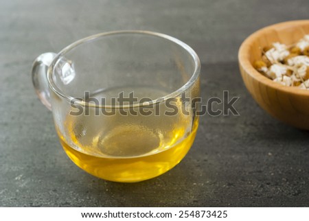 cup of chamomile tea with dried flowers on black wood table