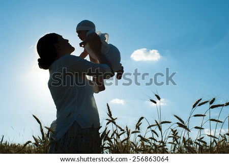 mother holding her baby on a wheat filed, silhouette