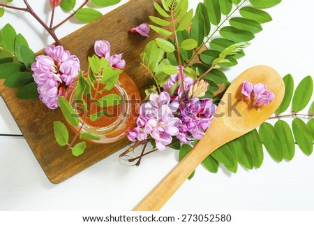 jar of natural robinia honey with acacia blossoms on white wood table