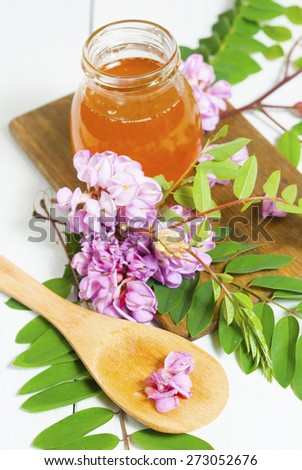 jar of natural robinia honey with acacia blossoms on white wood table