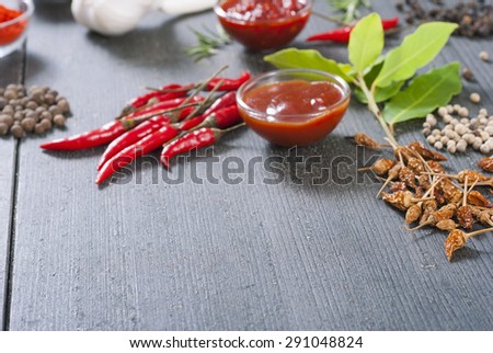 fresh and dried chili fruits, peppercorn, different acrid sauces and garlic, bay leaves on old black wooden table background