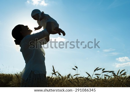 mother holding her baby on a wheat filed, silhouette