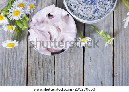 pink moisturizer cream, blue bath salt and white flowers on natural rusty wood table