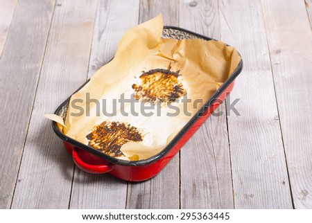 burned food prints on baking paper, old enamel frying pan on wooden table