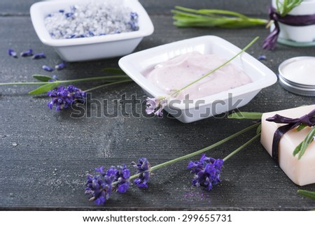 moisturizer cream, soap and bath salt with fresh lavender flowers on black wood background