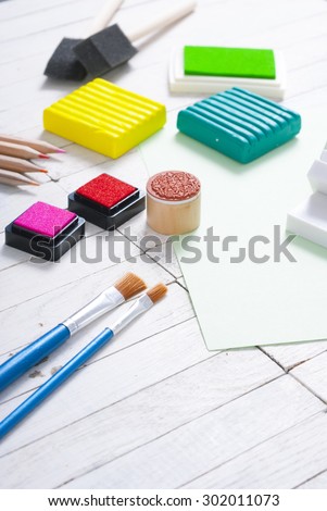 pencils, painting brushes, plasticine blocks and ink pads on white wood