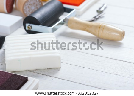 handicraft equipments, ink pads, lino cutter, paint roller and plasticine blocks on white wood table