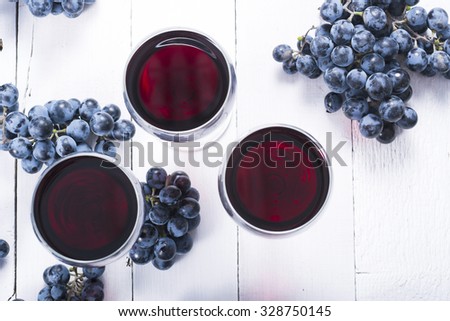 three glasses of red wine and blue grapes on white wooden table background