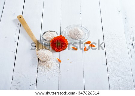 sea clay powder, moisturizer and bath salt with gerbera flower on white wooden table background