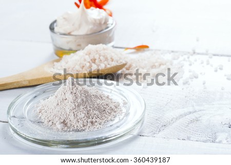 sea clay powder, moisturizer and bath salt with gerbera flower on white wooden table background