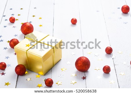 golden gift box with star shapes and red christmas balls on white wood table background