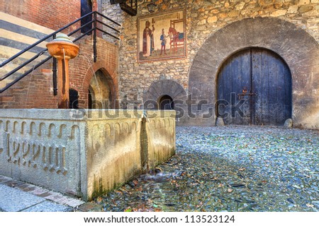 Interior court of Valentino Medieval Castle (aka Castello del Valentino) with ancient wooden door, small fountain and cobbled pavement in Turin, Italy.
