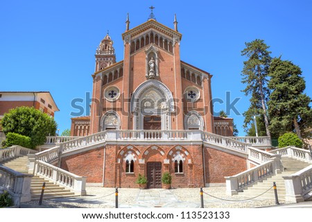 White stairs leading towards beautiful red catholic church under blue sky in Monforte D\'Alba, Piedmont, Northern Italy.