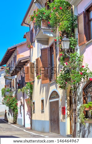 Vertical oriented image of typical italian house with balcony and blinds decorated with flowers in town of La Morra in Piedmont, Northern Italy.
