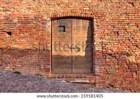 Red brick exterior wall of old house with wooden door on cobbled street in small italian town.