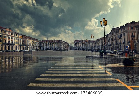 Pedestrian crossing and big plaza at city center under cloudy sky at rainy day in Cuneo, Italy.