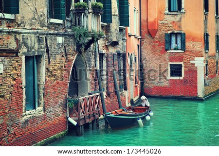 Small boat tied next to old red brick house with wooden balcony on narrow canal in Venice, Italy (toned image).