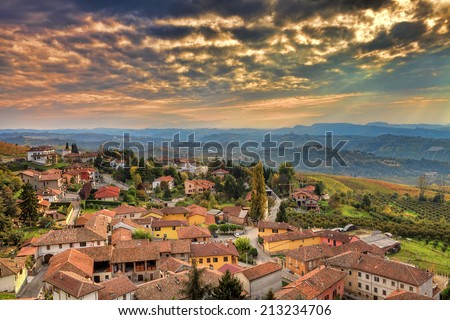 Small italian town among hills under beautiful cloudy autumnal sky at sunset in Piedmont, Northern Italy.