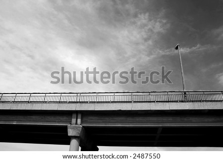 Street lamppost on transportation bridge under the cloudy sky as seen from below (black and white),