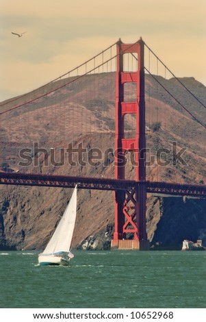 White yacht glides on water of San Francisco bay in front of Golden Gate Bridge.
