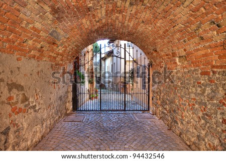 Old brick arched passage leading towards metal gate at the entrance to courtyard in La Morra, Italy.