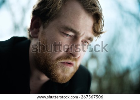 A portrait of a well dressed depressed man sitting on a bench in a park crying with a tear on his cheek.