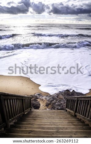 View from the high wood stairs on the wavy ocean with a white sun shining through the storm clouds, dramatic light  Bretagne,France