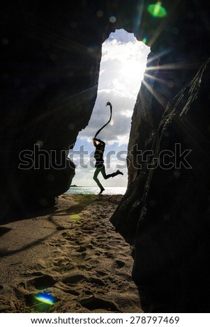 Happy woman with ribbon jumping on the beach in front of the cave entrance with sea and sky behind her