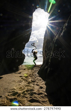 Happy woman with ribbon jumping on the beach in front of the cave entrance with sea and sky behind her