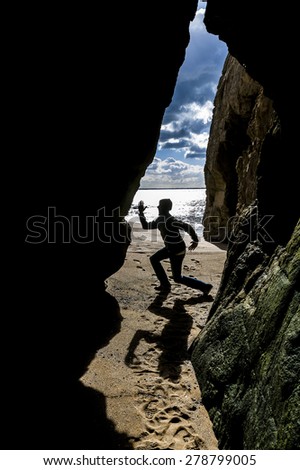Cave with man standing on a rock in front of the entrance with the sunny sky clouds and sea behind him