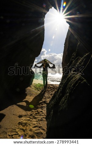 Happy woman with a scarf on her head standing on the beach in front of the cave entrance