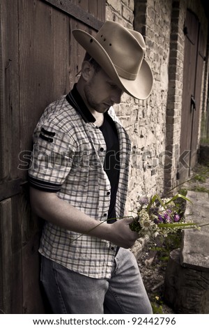 Young handsome sad man in cowboy hat standing with bunch of flowers