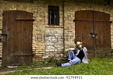 Young handsome country man sitting on the grass near the old shed