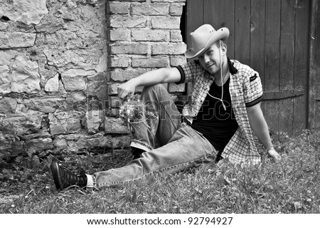 Handsome country man sitting on grass with flowers near the brick wall