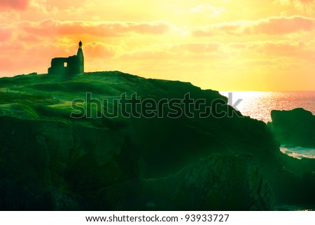 Silhouette of man on the sunrise standing on top of old ruined house on the hill near the ocean