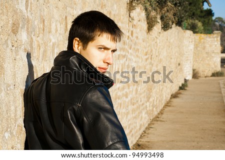 Young handsome man in black leather jacket is turning around and looking back seriously