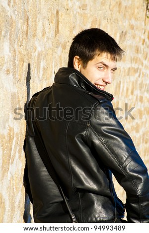 Young handsome man in black leather jacket is turning around and winking with happy smile
